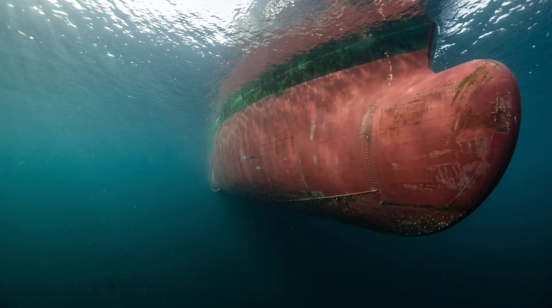 The bow of a tanker seen from below the surface, against the light